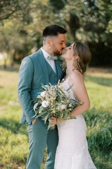 Couple de mariés s’embrassant dans un jardin, la mariée tenant son bouquet