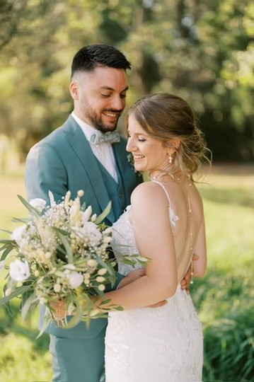 Couple de mariés souriant dans un jardin, la mariée tenant son bouquet