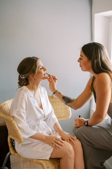 Laura maquille les lèvres d’une future mariée assise en peignoir blanc