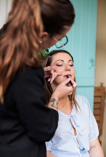 Laura maquille les lèvres d’une cliente pendant sa préparation