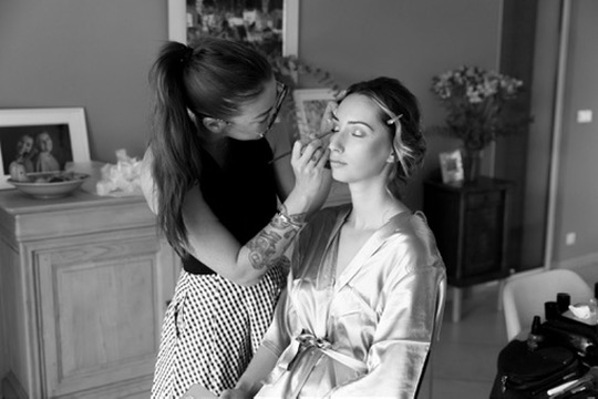 Laura maquille une cliente pendant sa préparation, en noir et blanc