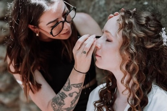 Laura maquille les yeux d’une cliente aux cheveux bouclés en extérieur